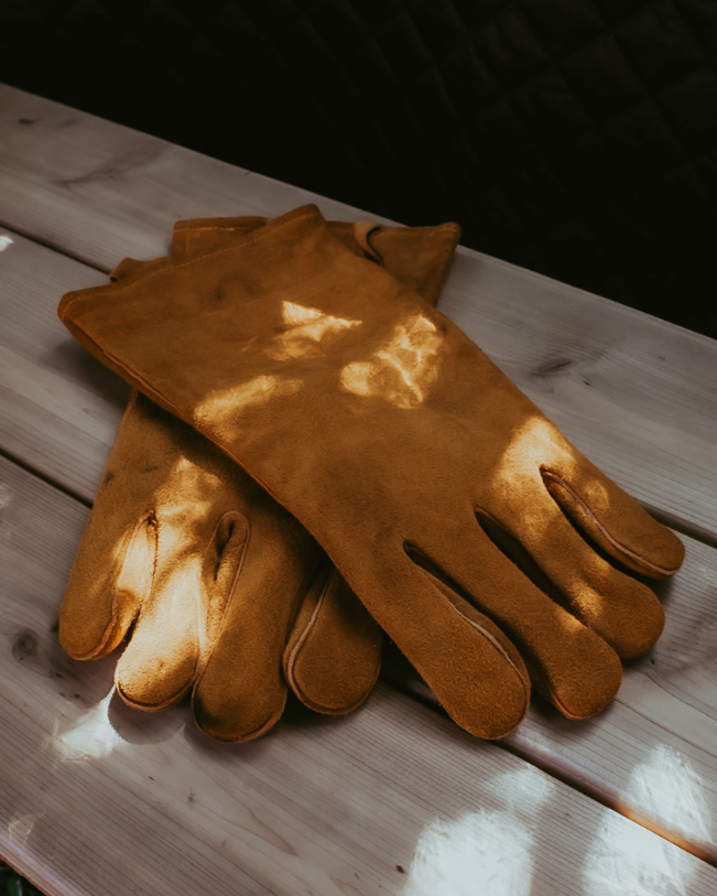 Pair of brown leather gloves on a wooden surface with a dark background