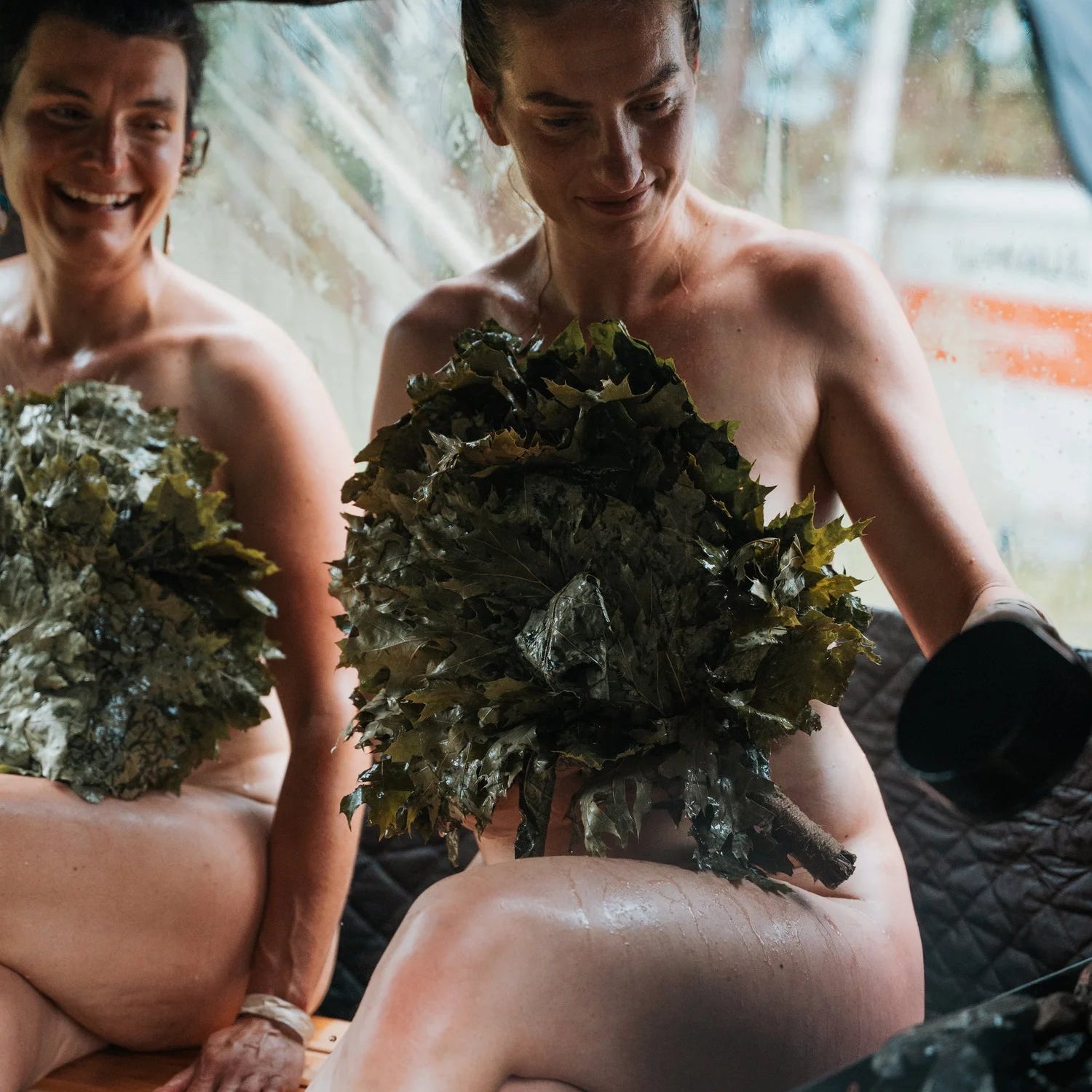 Two people sitting under a tent with plants on their bodies.