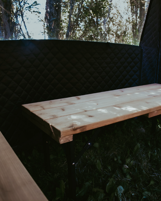 Wooden sauna benches in a Themaculture sauna tent in a forest setting with trees in the background