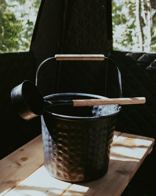 Black metal bucket with wooden handle on a wooden surface with blurred greenery in the background