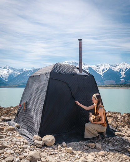 Thermaculture portable sauna tent used outdoors by a lake, wood-fired sauna setup with mountain scenery.