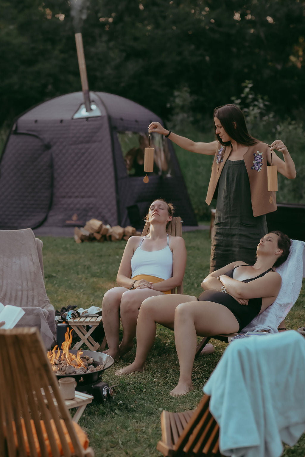 Two women sitting by a campfire with a tent in the background